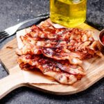 Pieces of fried bacon on a wooden cutting board.