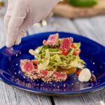 Chef hands sprinkling sesame on salad with tuna